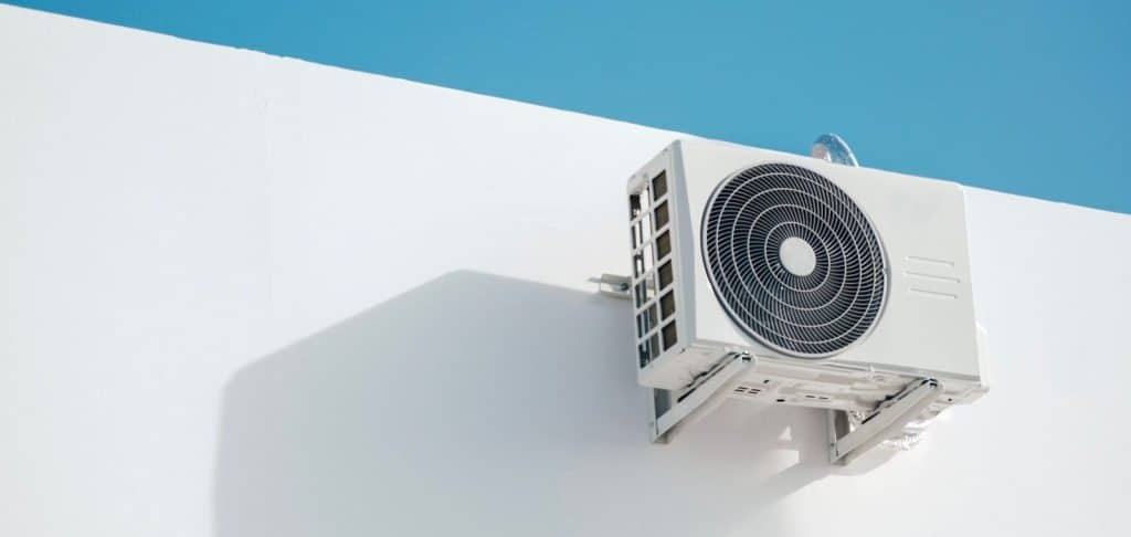 White outdoor mini-split condenser mounted on a white wall against a clear blue sky